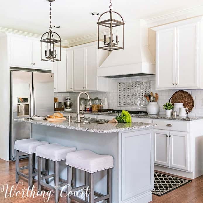 Kitchen with white shaker cabinets, gray island, large hood and stainless refrigerator details.