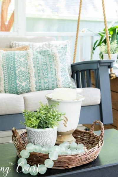 Vignette in a basket on a coffee table with a porch swing and side table in the background