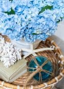 blue hydrangeas in a white vase in a wicker tray on coffee table