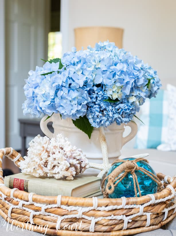 Seashells, a book, flowers and blue glass in the vignette on the coffee table.