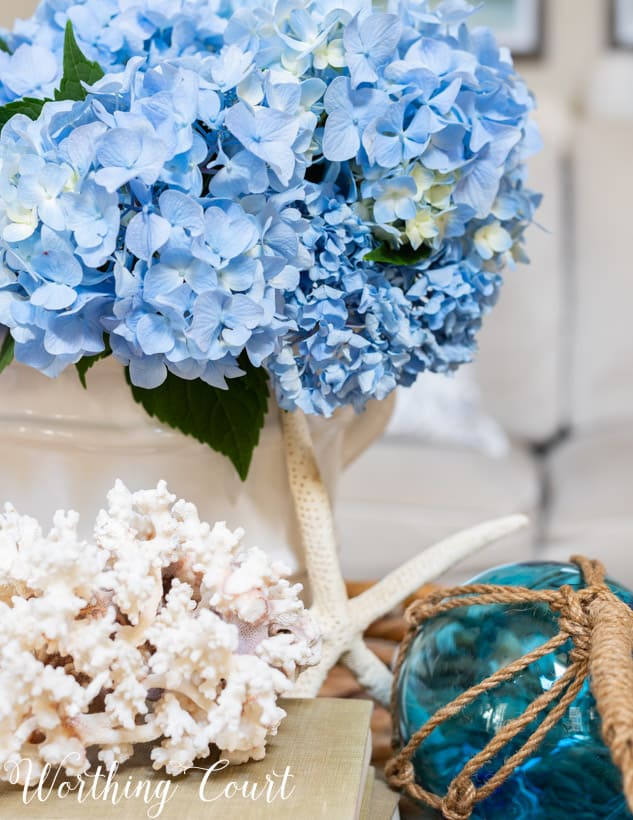 blue hydrangeas in a white vase in a wicker tray on coffee table.