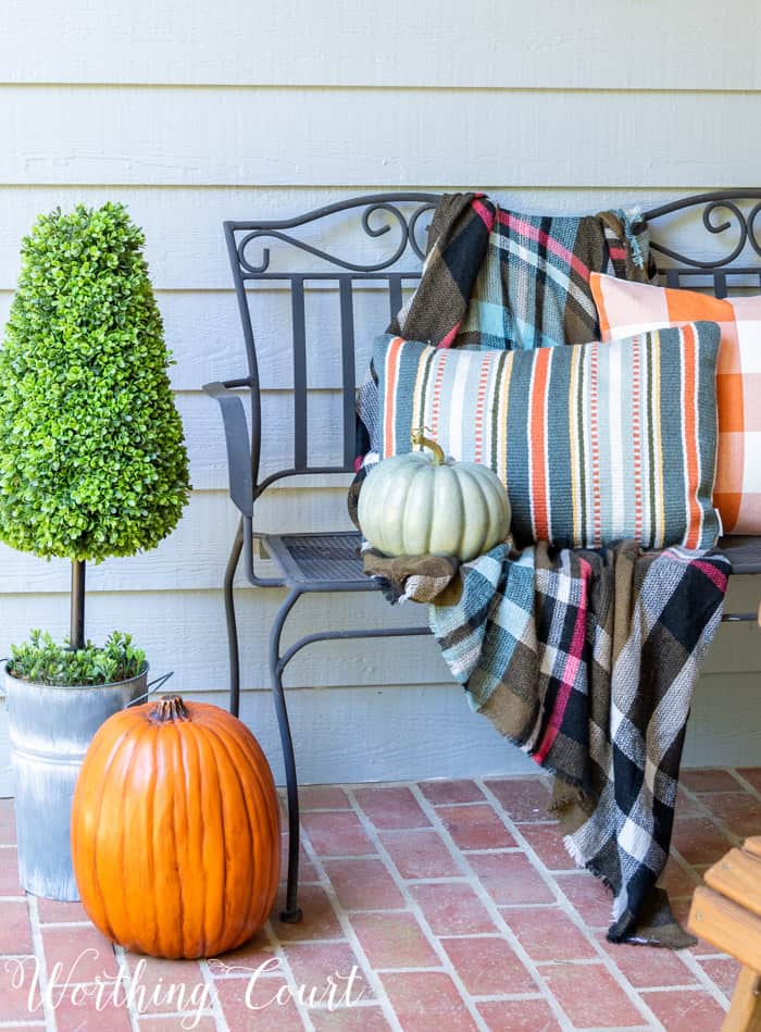black outdoor bench with fall pillows and pumpkins