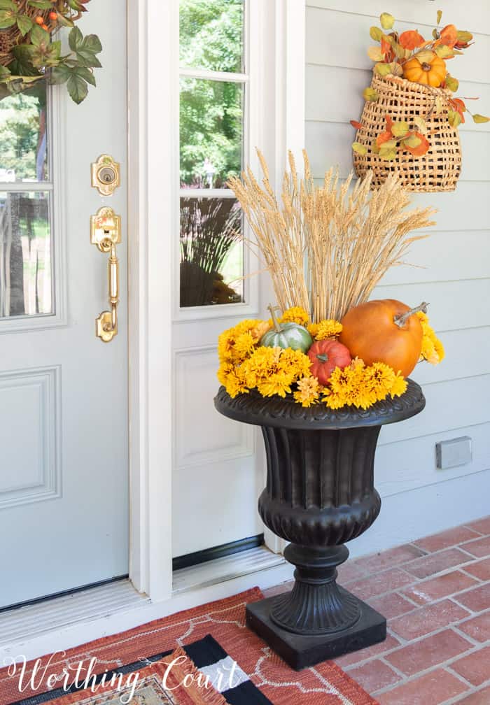 black urn filled with mums, pumpkins and wheat