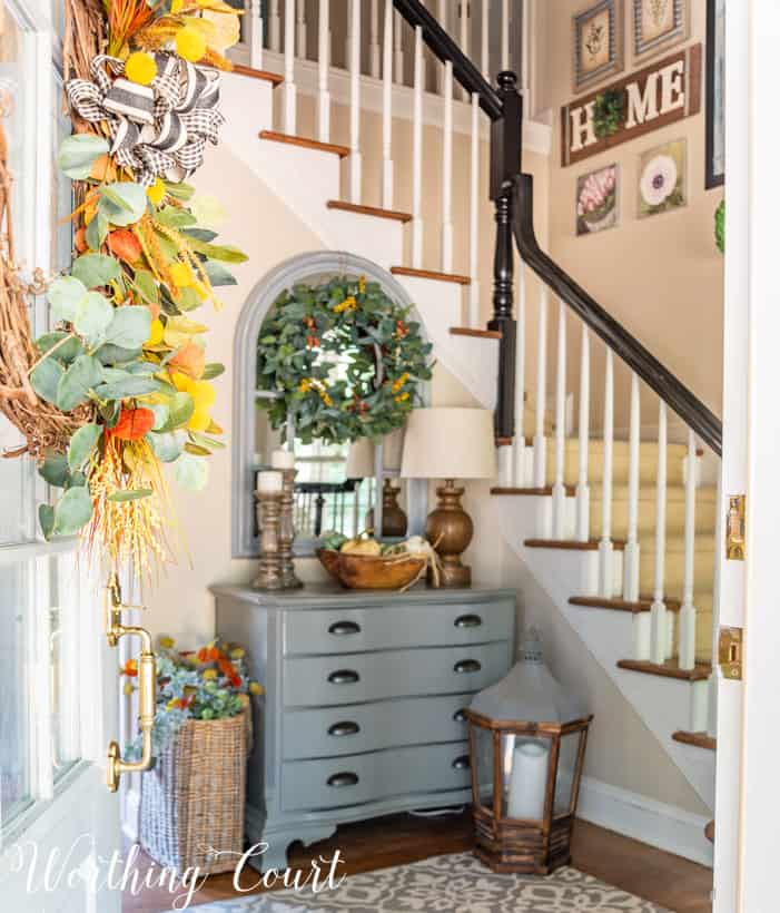 gray chest in foyer with L shaped stairway and fall decor