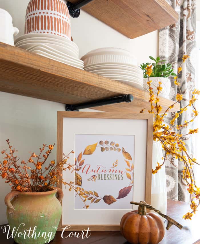 free printable with fall saying and colors displayed in a frame on a sideboard