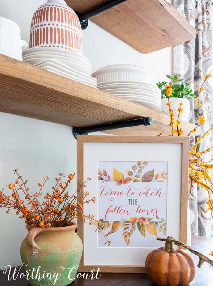 free printable with fall saying and colors displayed in a frame on a sideboard