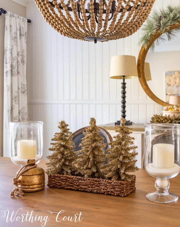 Christmas centerpiece with tinsel trees in a wicker basket, glass candle holders and a gold bell