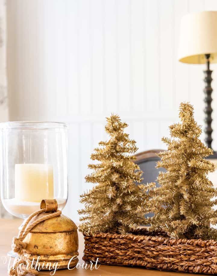 Christmas centerpiece with tinsel trees in a wicker basket, glass candle holders and a gold bell