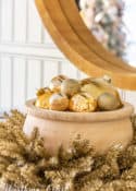 wood bowl filled with gold Christmas ornaments nestled in a tinsel wreath