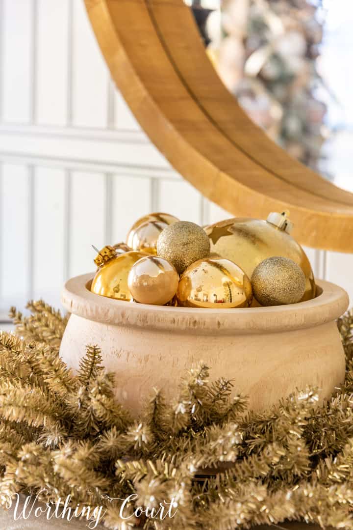 wood bowl filled with gold Christmas ornaments nestled in a tinsel wreath