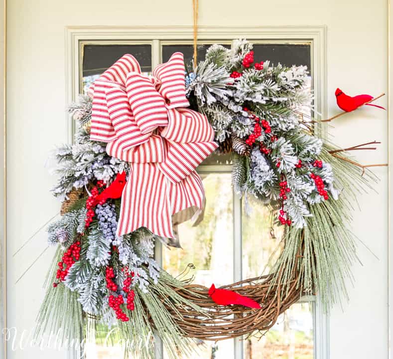 Christmas wreath with flocked pine branches, red cardinals and red and white striped ribbon