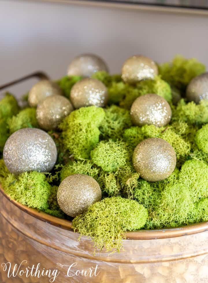 gold metal bowl filled with green moss and gold Christmas ornaments