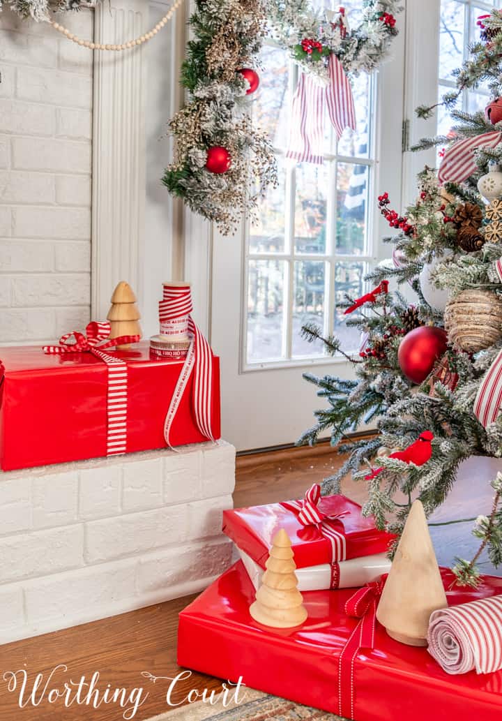 Christmas presents in red wrapping paper with red and white ribbon beside Christmas tree