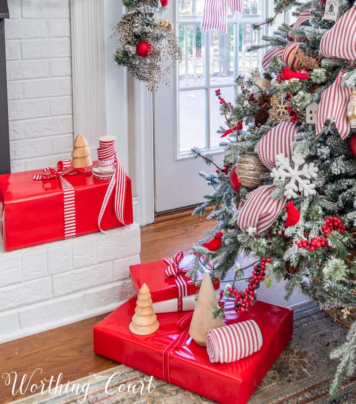 Christmas presents in red wrapping paper with red and white ribbon beside Christmas tree