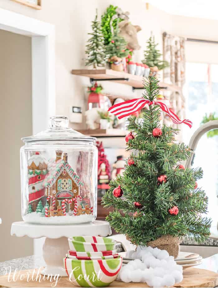 Christmas vignette with glass canister, mini tree, mini house on a cake pedestal