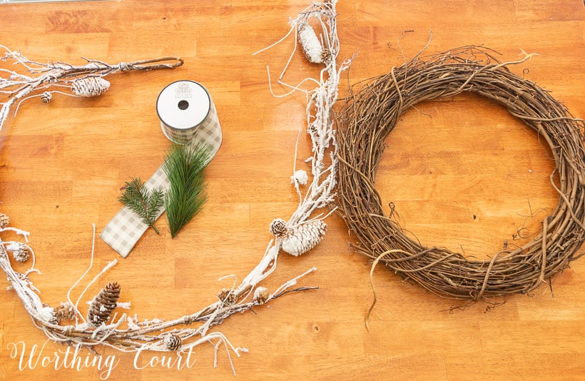 grapevine wreath, snowy garland, faux pine pieces and ribbon laying on a wood table