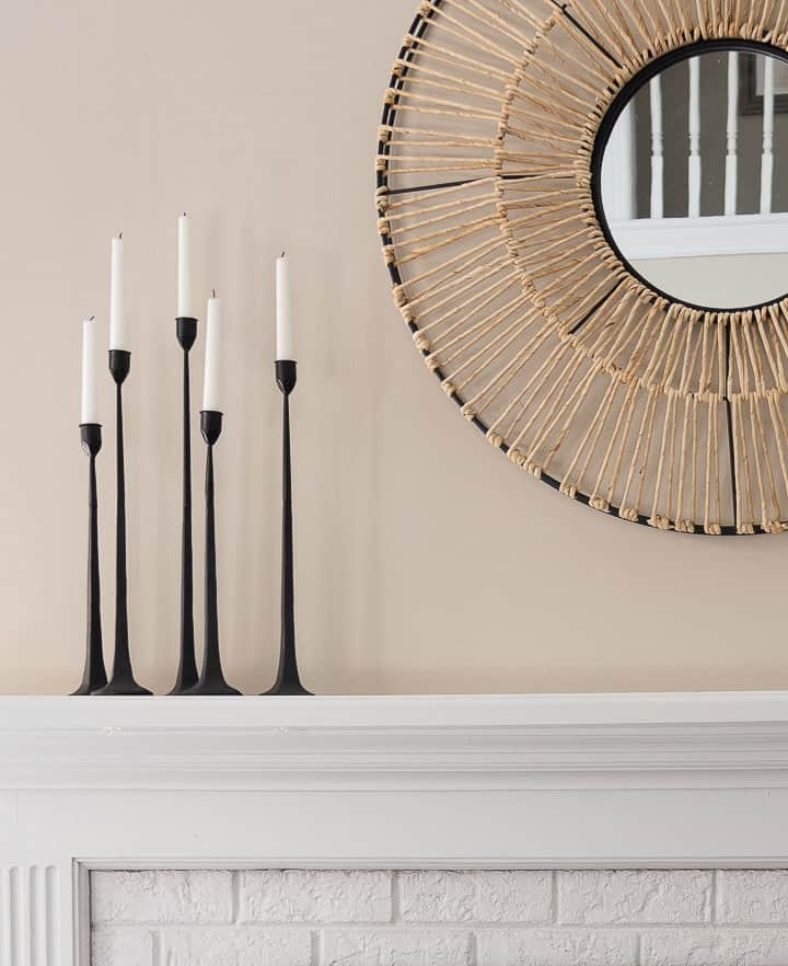 grouping of black candlesticks beside a white mirror on a white fireplace mantel