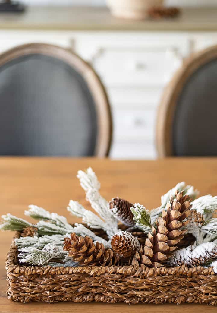 faux snow covered pine branches and pinecones in a small wicker basket on a dining table