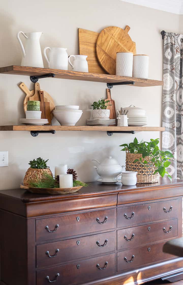 open shelves above wood sideboard decorated for winter with white dishes