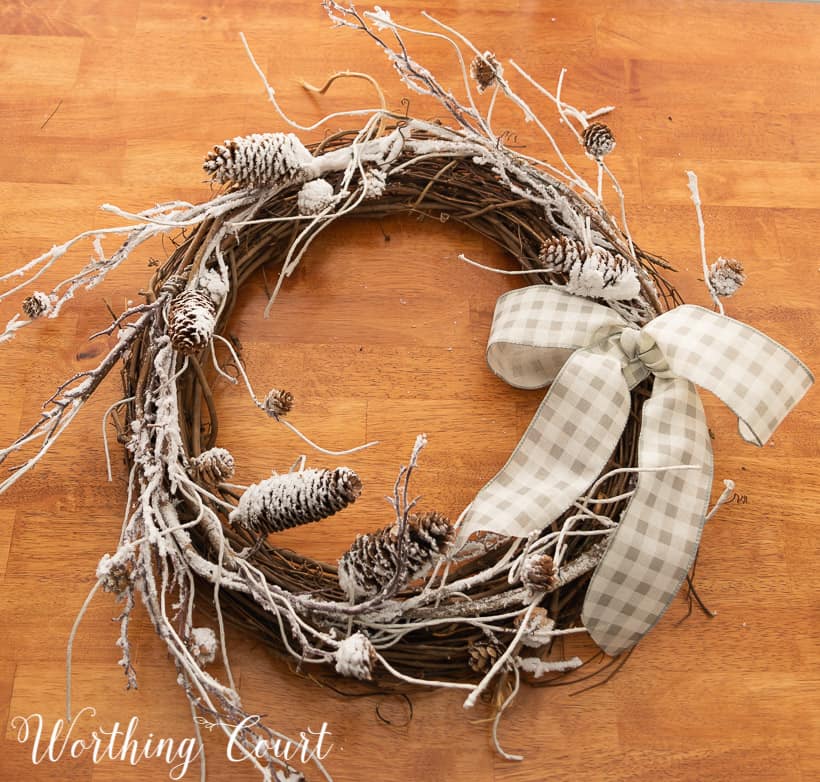 in process photo of the making of a wreath with snowy branches, pinecones and a bow