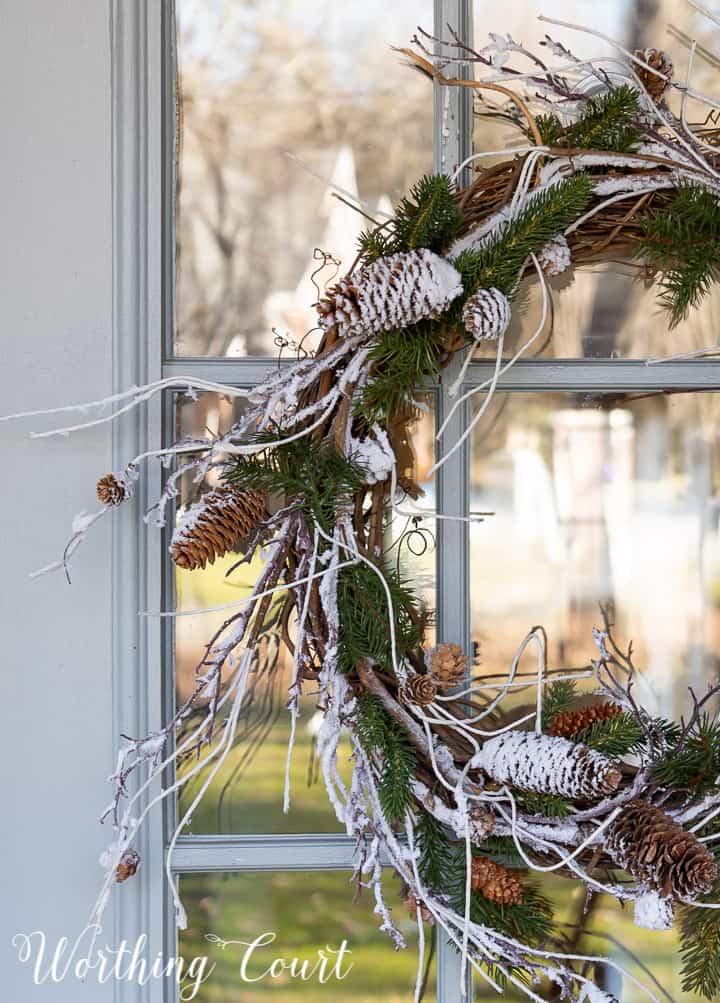 winter wreath with snow and pine branches and pinecones with a bow hanging on a glass door