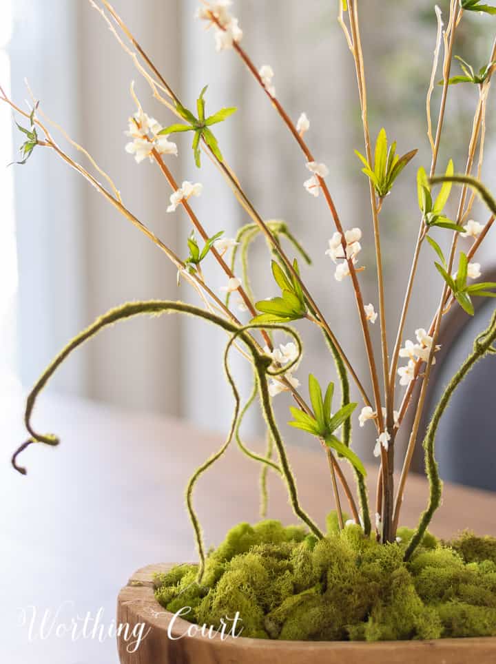 wood bowl filled with green moss and tall faux greenery