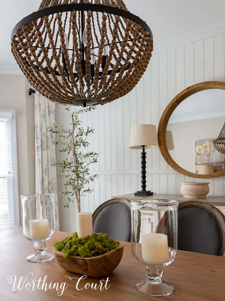 wooden bowl filled with green moss and a single white candle in the center of a dining table