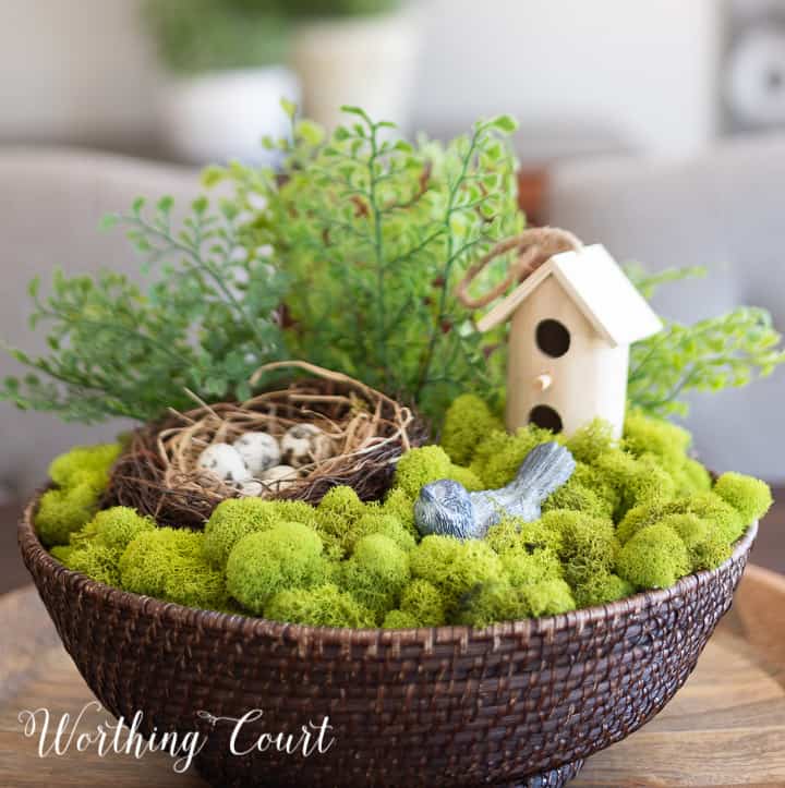 wicker bowl filled with green moss, faux greenery, a nest and faux bird
