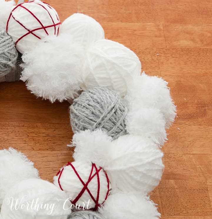 Partial view of Valentine's Day wreath made with styrofoam balls covered with white and gray yarn and a heart cutout wrapped with red yarn