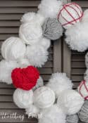 Partial view of Valentine's Day wreath made with styrofoam balls covered with white and gray yarn and a heart cutout wrapped with red yarn