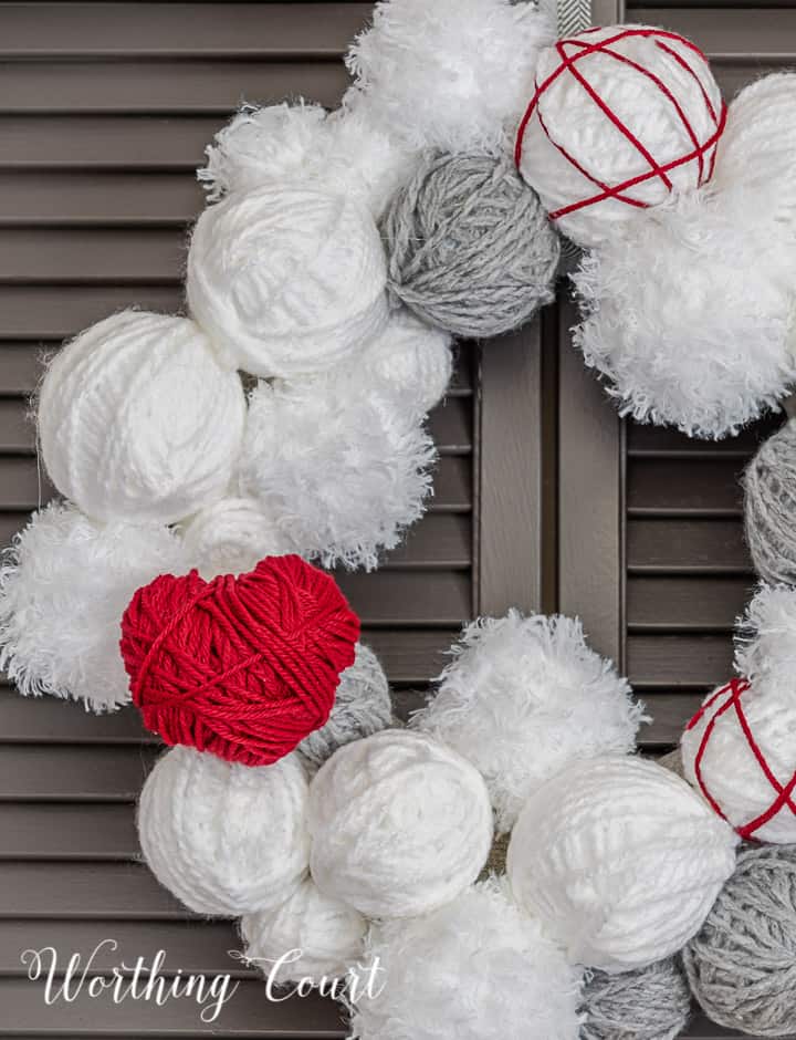 Partial view of Valentine's Day wreath made with styrofoam balls covered with white and gray yarn and a heart cutout wrapped with red yarn