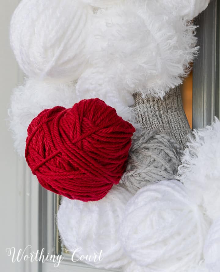 Partial view of Valentine's Day wreath made with styrofoam balls covered with white and gray yarn and a heart cutout wrapped with red yarn