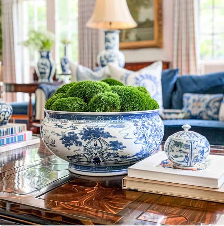 blue and white chinoiserie bowl filled with moss ball orbs on a coffee table with other blue and white accessories in a living room