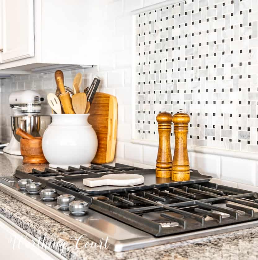 wood salt and pepper mill and marble spoon rest on top of burner griddle and other decorative items on countertop