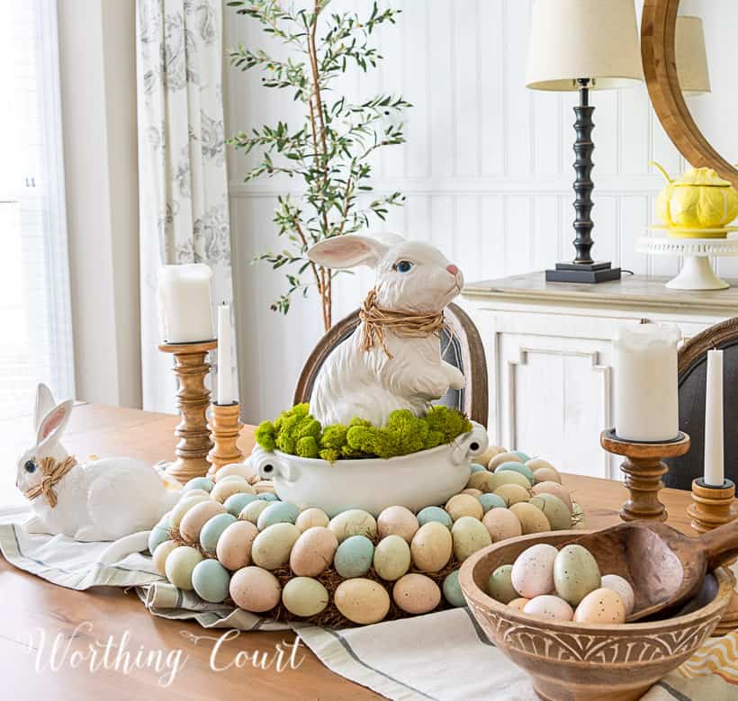 Easter centerpiece with white ceramic bunny in the middle of an egg wreath and a wood bowl filled with faux Easter eggs