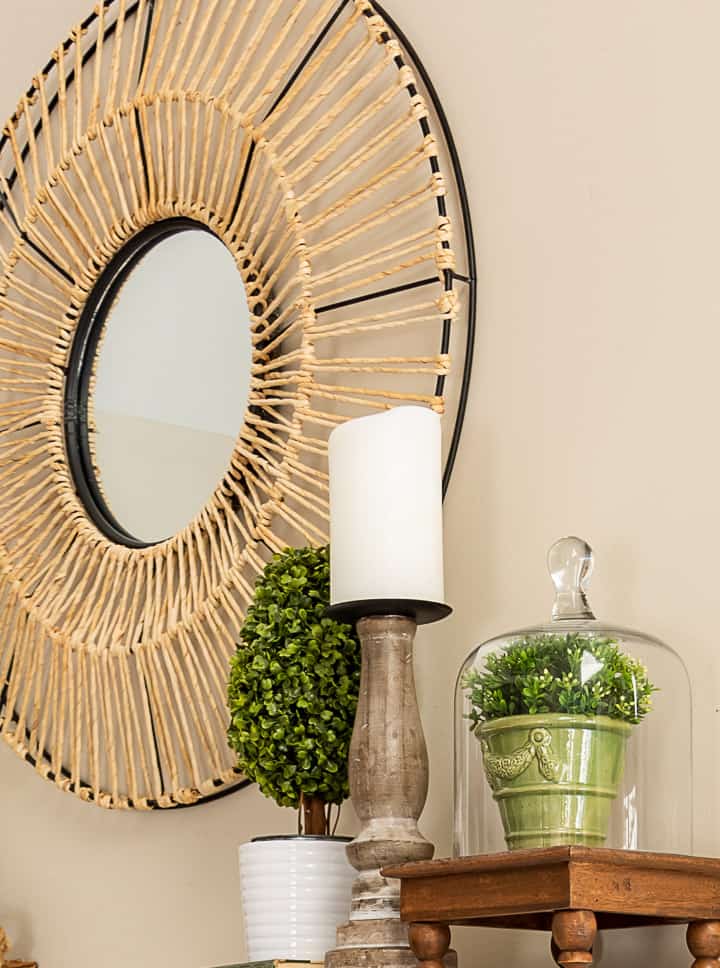 spring vignette with a topiary, candle and small plant under a glass cloche with a round mirror in the background