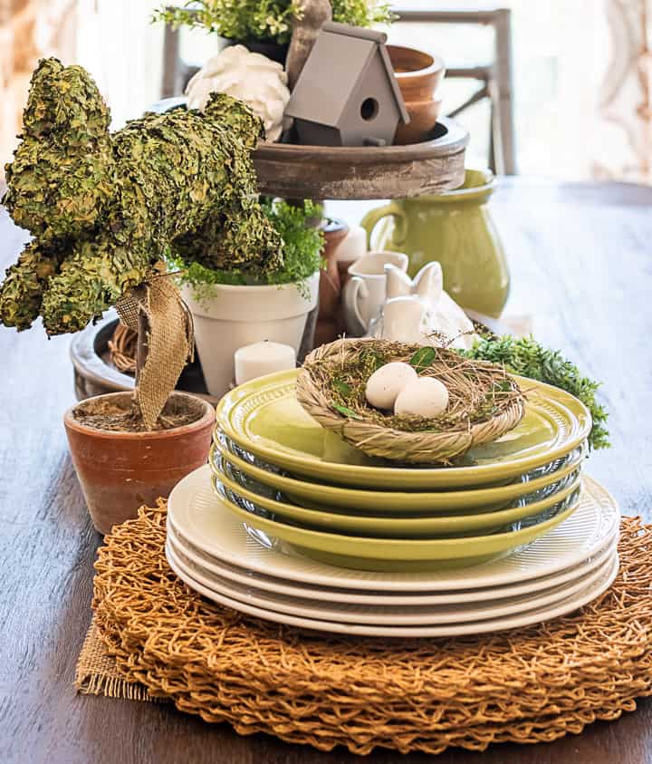 portion of a spring centerpiece with stacked green and white plates and a bunny topiary