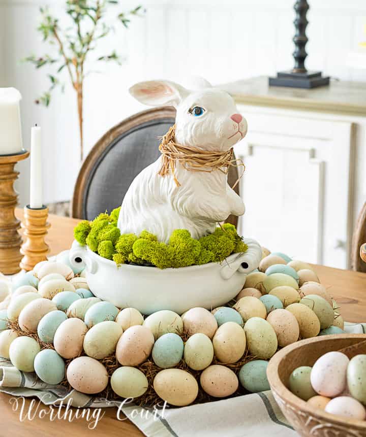 Easter centerpiece with white ceramic bunny in the middle of an egg wreath and a wood bowl filled with faux Easter eggs