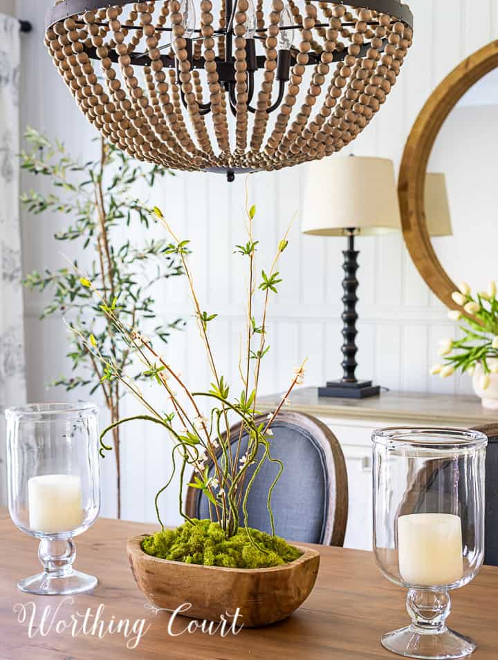 Mesa de comedor neutral con sillas laterales grises y aparador blanco con decoración de primavera