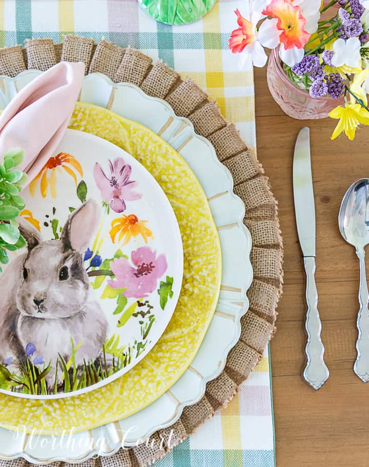 Easter place setting with burlap placemat topped with a charger, yellow plate and bunny salad plate