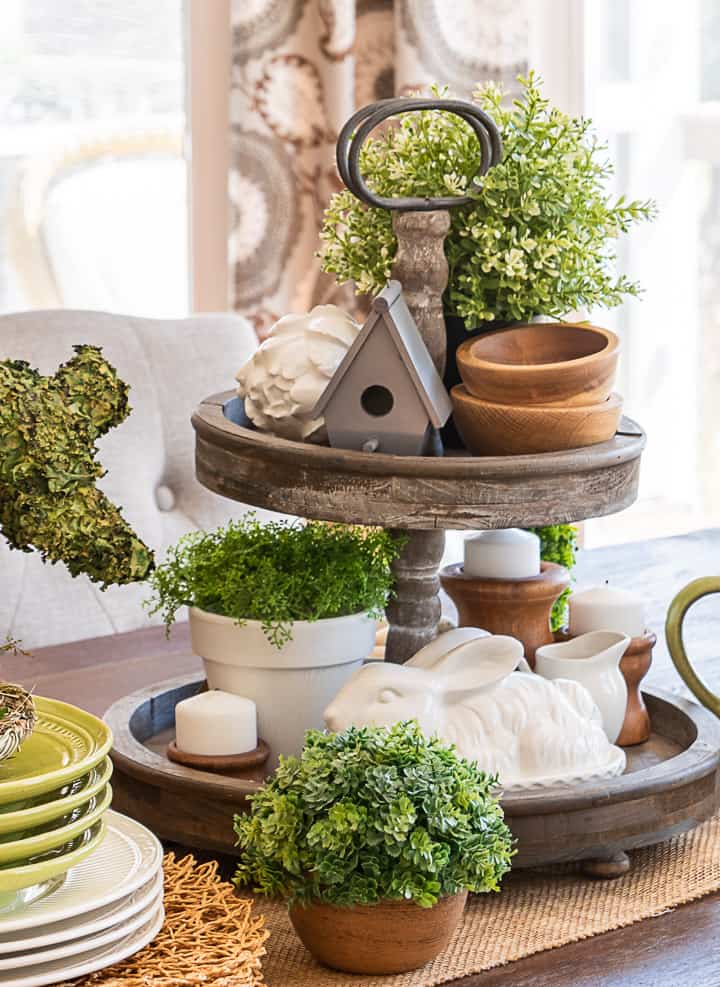 tiered tray decorated for spring with greenery, a birdhouse, candles and a bunny