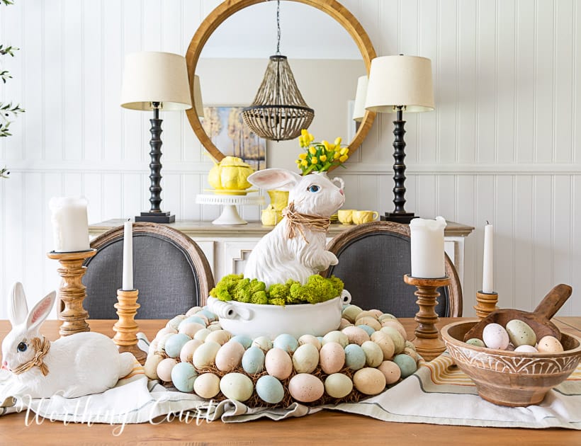 Easter centerpiece with white ceramic bunny in the middle of an egg wreath and a wood bowl filled with faux Easter eggs