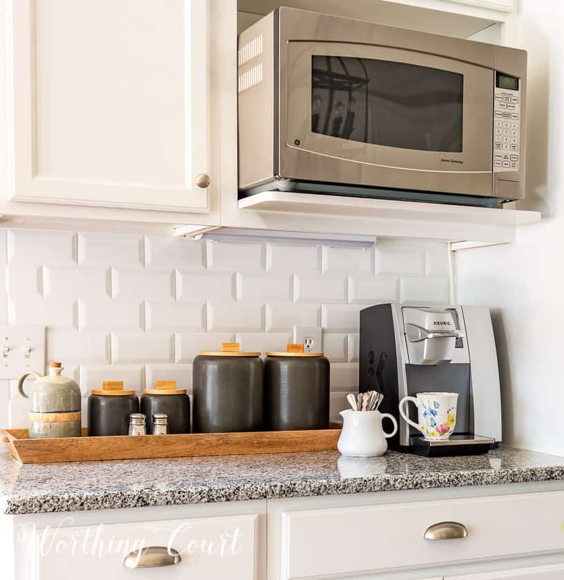 gray canisters and coffee maker in a kitchen with white cabinets and subway tile backsplash