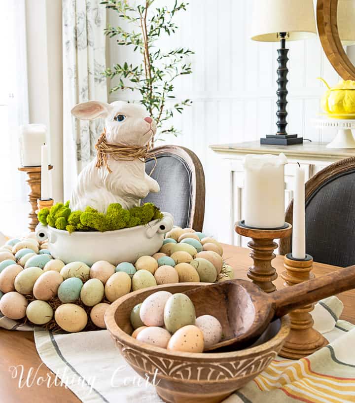 Easter centerpiece with white ceramic bunny in the middle of an egg wreath and a wood bowl filled with faux Easter eggs