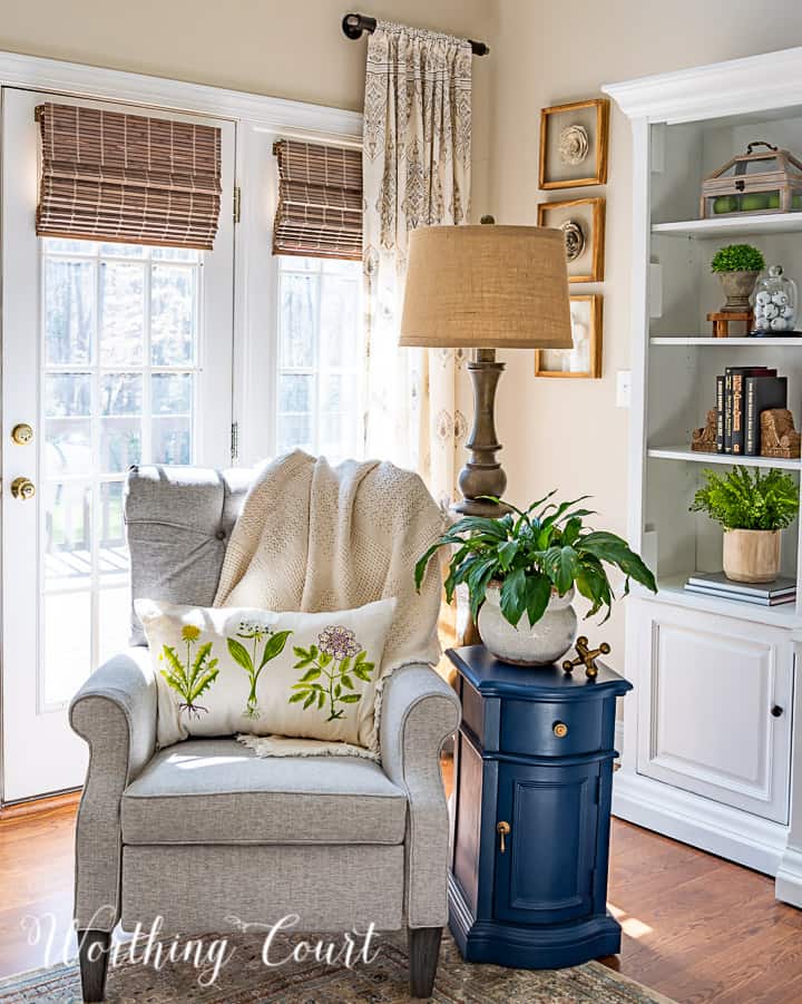 Silla gris con una fragancia con una lámpara de piso y una mesa lateral azul con una almohada de resorte y una planta viva