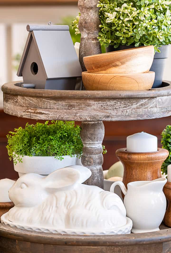 tiered tray decorated for spring with greenery, a birdhouse, candles and a bunny