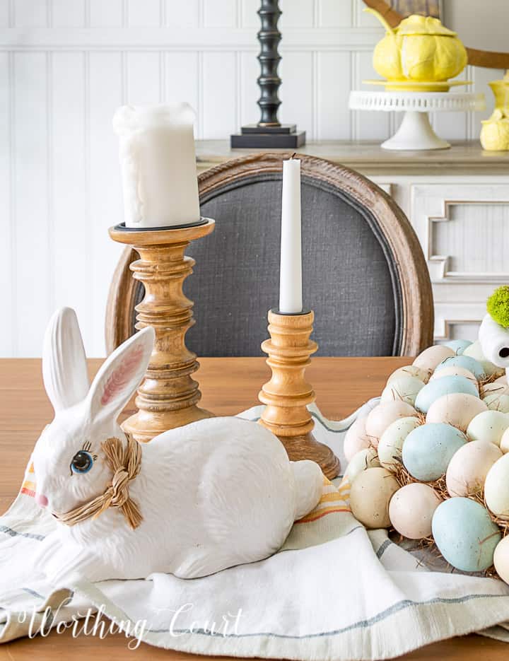 White ceramic bunny and wood candlesticks with white candles in an Easter centerpiece