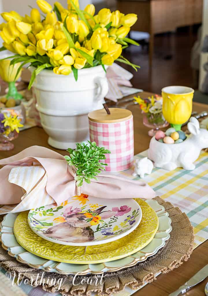 Easter place setting with burlap placemat topped with a charger, yellow plate and bunny salad plate