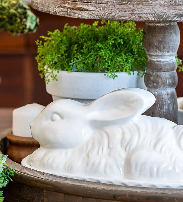 bottom level of a tiered tray with a white bunny and faux greenery