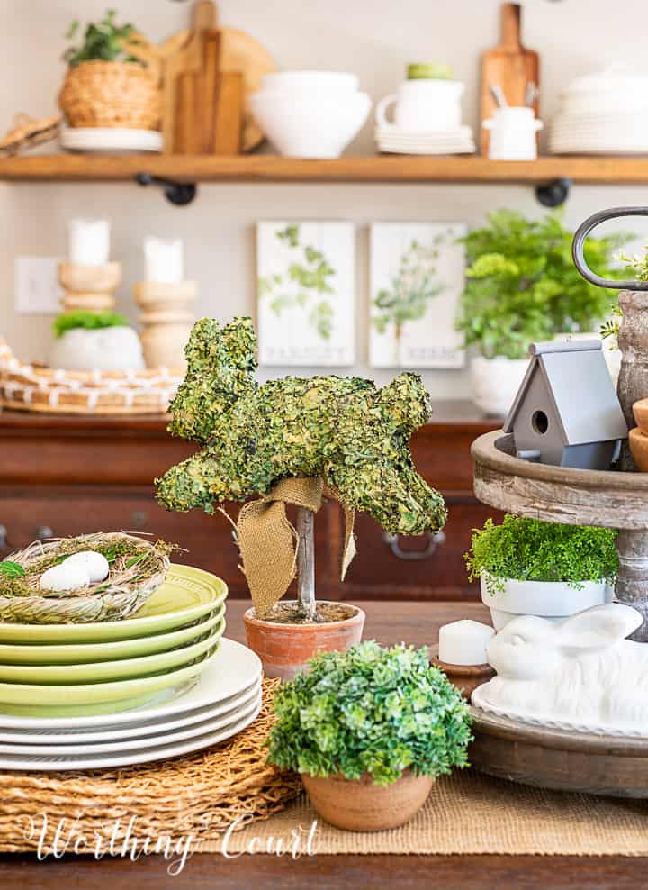 portion of a spring centerpiece with bunnies, greenery and white accessories and dishes